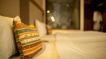 Un cuarto de hotel con una cama bien hecha, una almohada colorida y una ventana con vista a la ciudad.