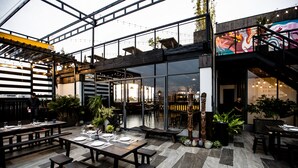 Un espace de restauration intérieur avec des tables et des bancs en bois, de grandes fenêtres et un escalier menant à un niveau supérieur.
