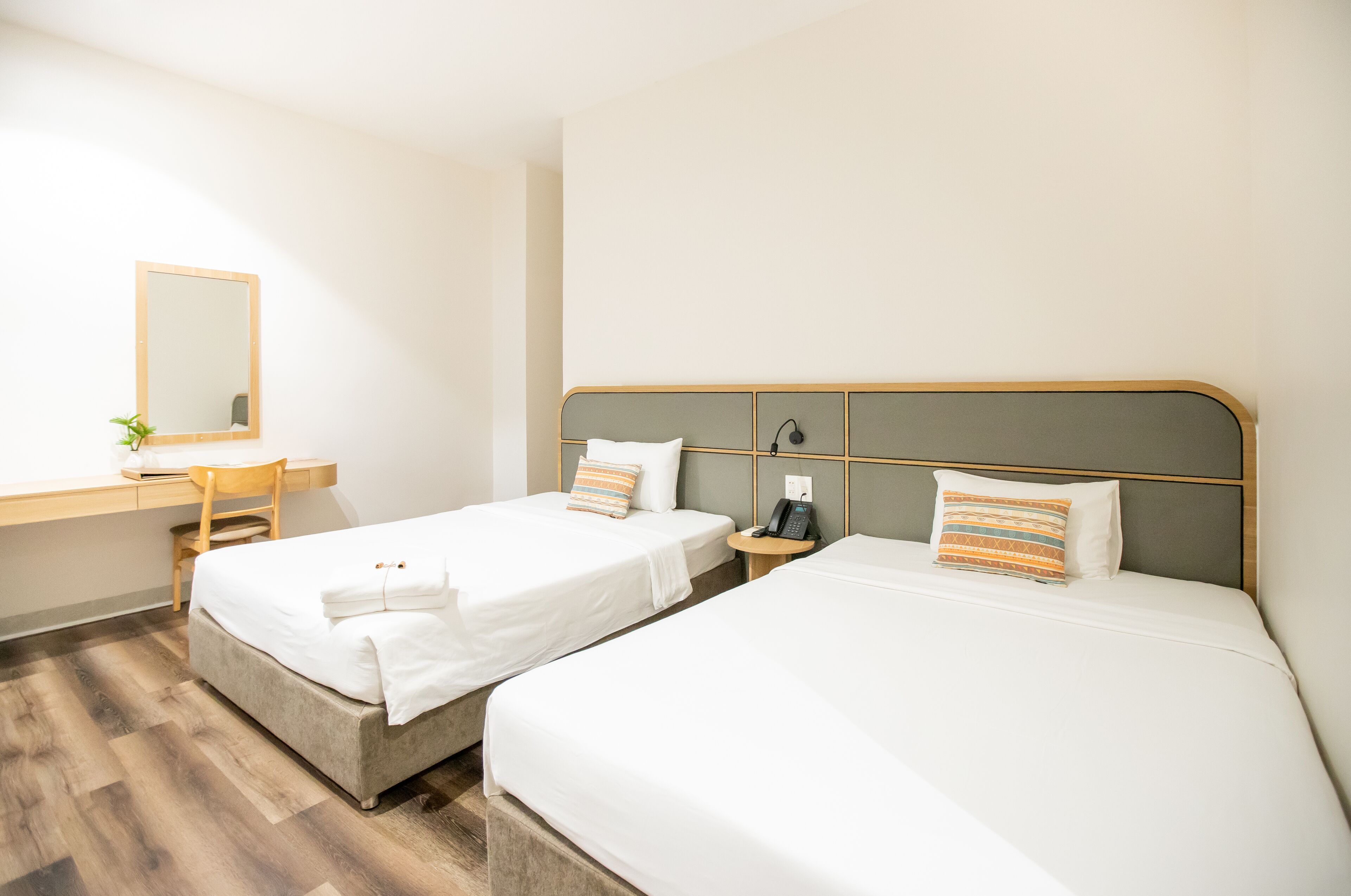 A hotel room with two beds, a desk, a chair, a bedside table with a phone, and a mirror.