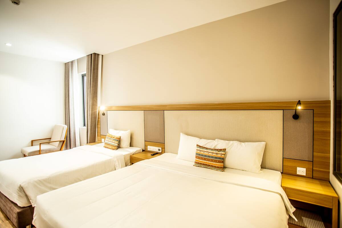 A hotel room with two beds, a chair, and a nightstand with a lamp.