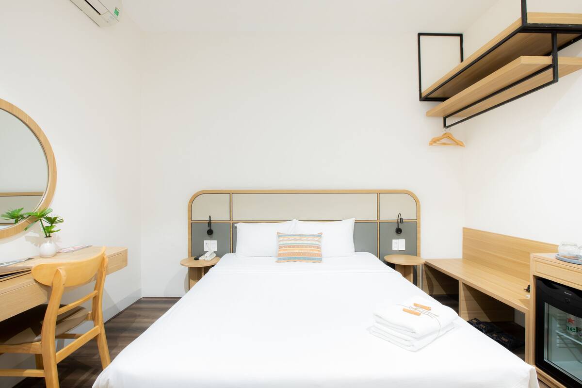A hotel room with a bed, a desk, a chair, a mirror, a nightstand, and a TV.