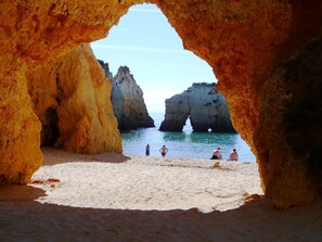 A beach scene framed by natural rock formations with clear water and a few people in the distance. - Apartment Centianes Sol (Carvoeiro)