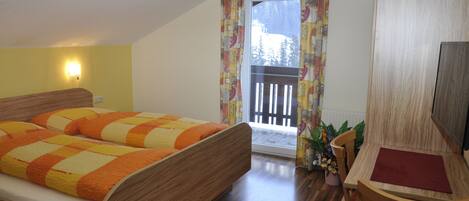 Ein Schlafzimmer mit einem hölzernen Bett, einem kleinen Tisch mit einer roten Unterlage und einem Fenster mit Blick auf eine verschneite Landschaft.
