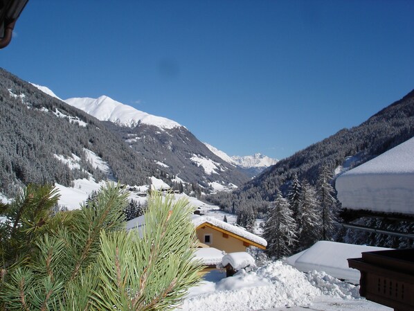 A mountain cabin with a snow-covered roof, surrounded by pine trees and snow-covered mountains.