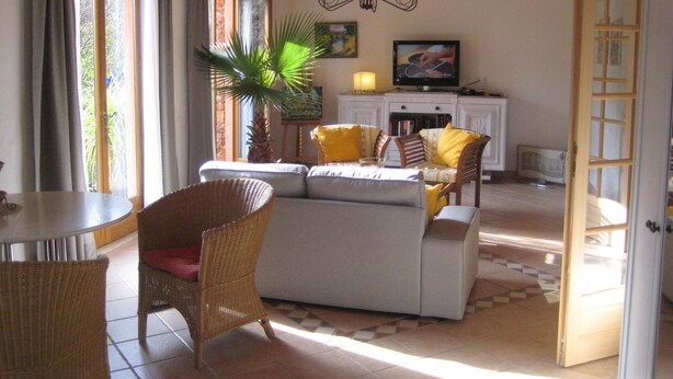 Ein Wohnzimmer mit Sofa, Sesseln, einem Esstisch, einer Kronleuchter und einem Fernseher.