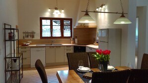 Eine Küche mit Esstisch für zwei Personen, einem Kühlschrank und einem Fenster mit Vorhängen.