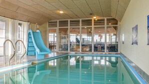 An indoor swimming pool with a blue slide, glass walls, and a view of the dining area. - Nice home in Harboøre with kitchen (Harboøre)