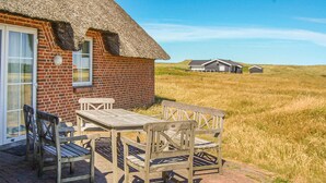 A thatched-roof cottage with a brick exterior, a wooden table and chairs, and a view of the surrounding grassy landscape. - Nice home in Harboøre with kitchen (Harboøre)