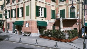 A multi-story building with green shutters, a visible ground floor entrance, and a small outdoor seating area.