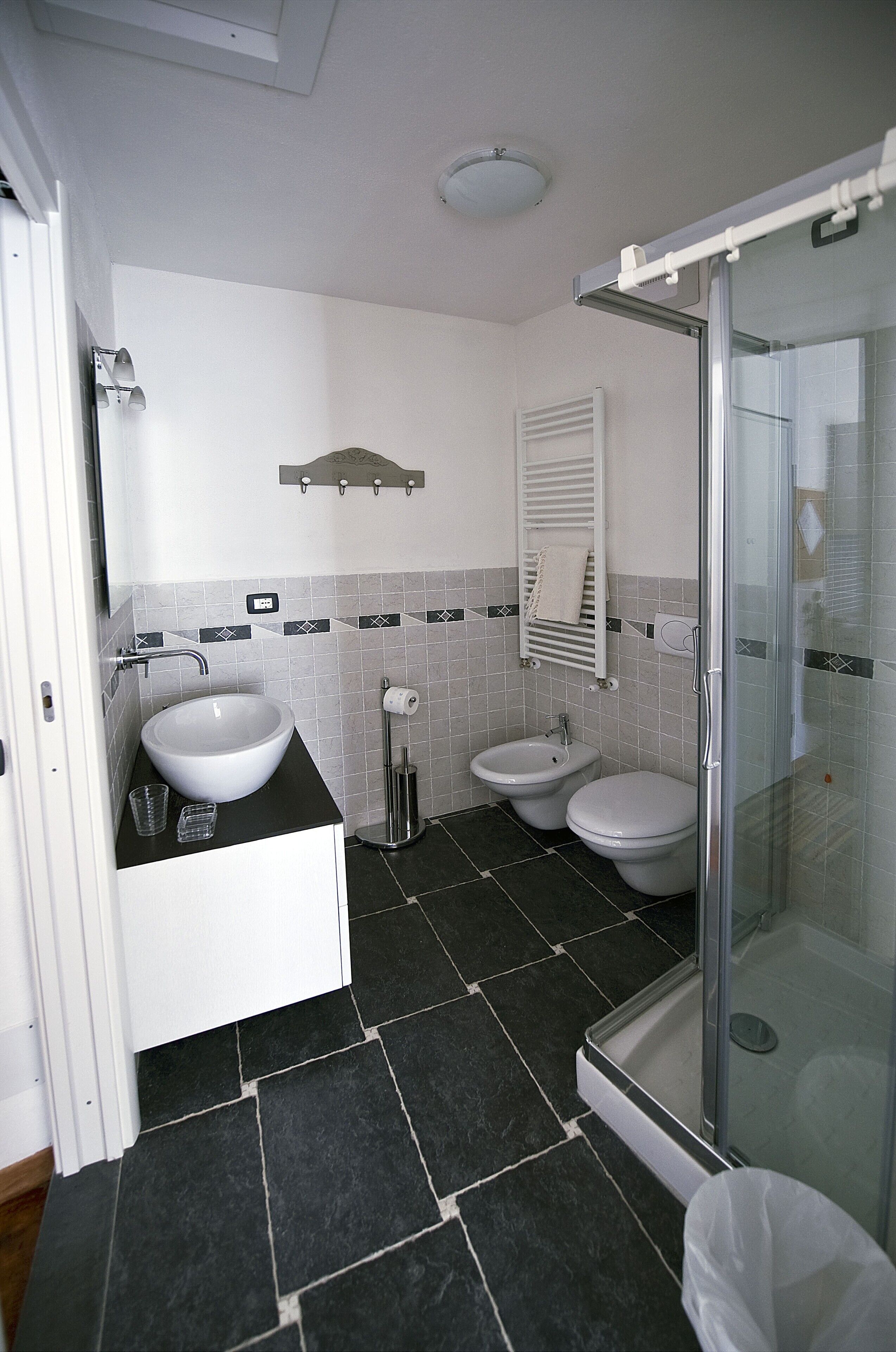 A modern bathroom with a white sink, two toilets, a bidet, and a glass-enclosed shower.