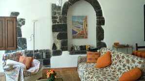 A cozy living room with a stone archway, a sofa with floral upholstery, a wooden cabinet, and a bookshelf with books.