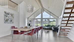 Àmplia zona de dinar amb una taula llarga i cadires vermelles, un llum modern i vistes a l'exterior a través de grans finestres.