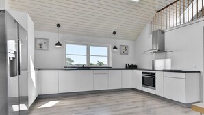 Cuina moderna amb armaris blancs, nevera d'acer inoxidable, forn integrat i finestra que proporciona llum natural.
