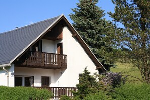 Eine zweistöckige Chalet mit Balkon, umgeben von Grün und Bäumen.