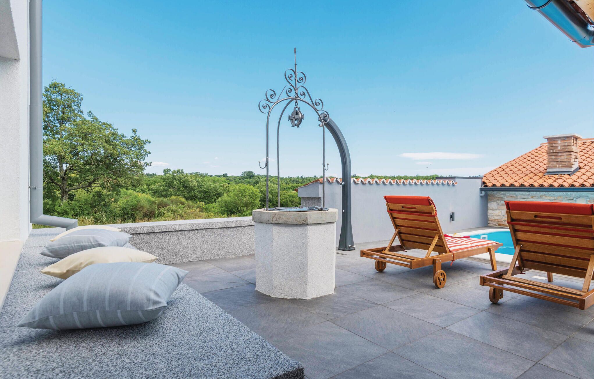 A rooftop terrace with a pool, two wooden lounge chairs, and a stone bench with cushions.