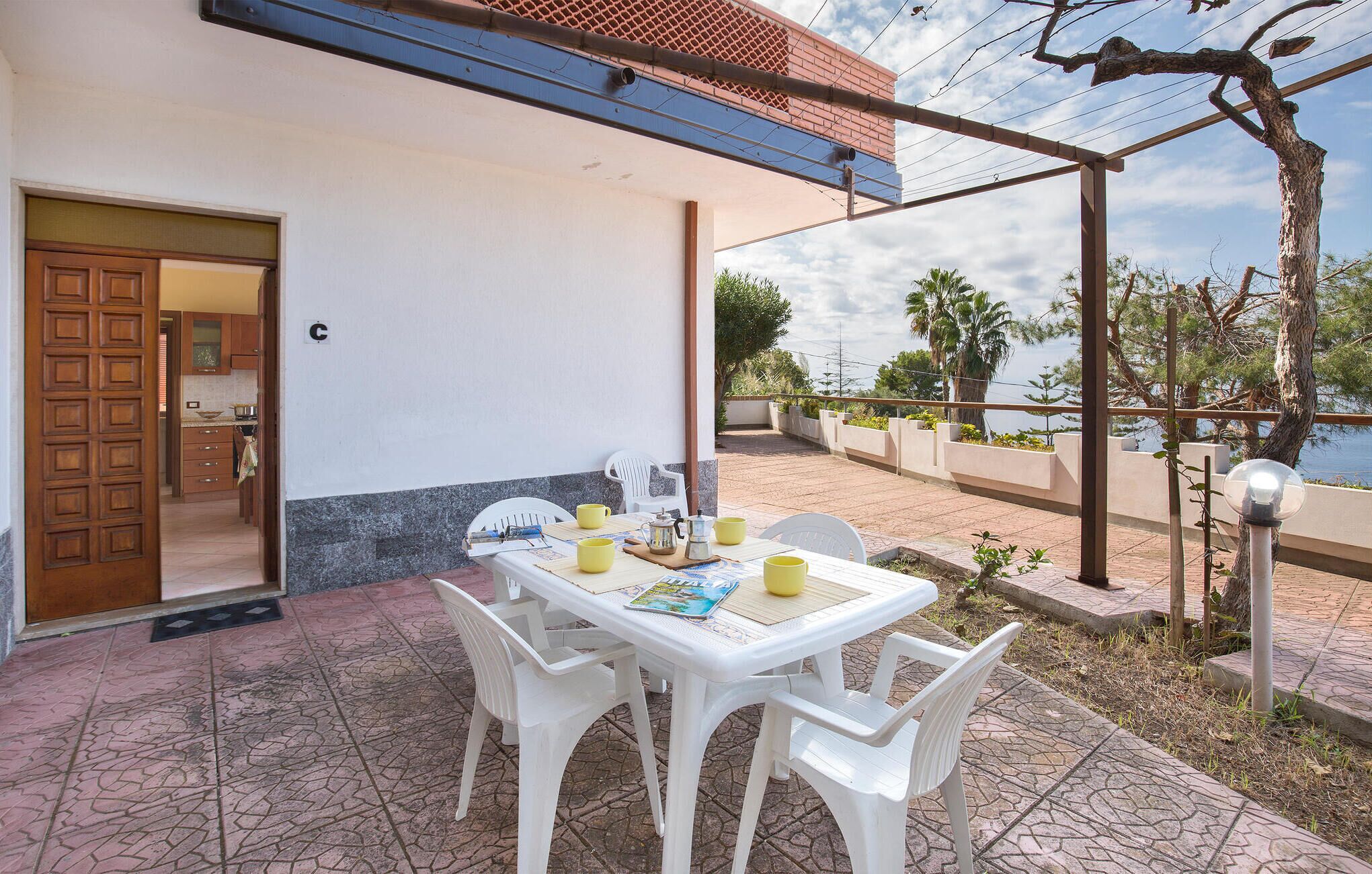 Eine Terrasse mit Tisch für zwei Personen, weißen Plastikstühlen und Blick aufs Meer.