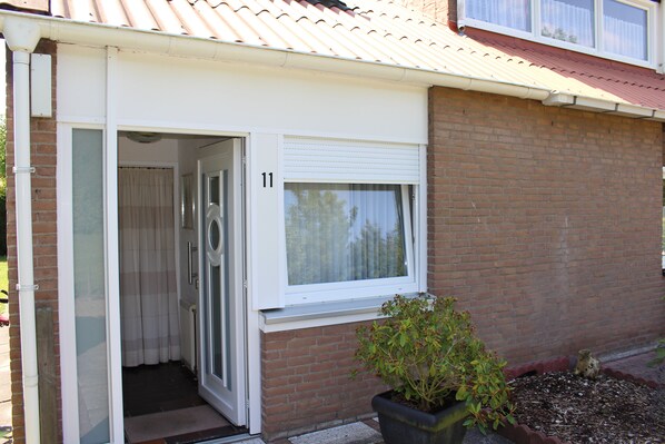 A residential building with a number 11, a sliding glass door, a window with a white blind, and a potted plant in front. - Cozy holiday home on the Grevelingenmeer (Bruinisse)