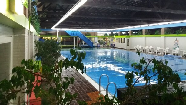 Una piscina interior con superficie de agua azul, rodeada por un solado de azulejos.