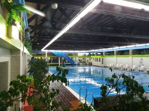 Une piscine intérieure à l’eau bleue, entourée d’une terrasse carrelée.
