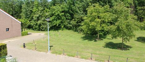 A paved driveway leading to a building with a brick facade, surrounded by a grassy area with trees and a lamp post.