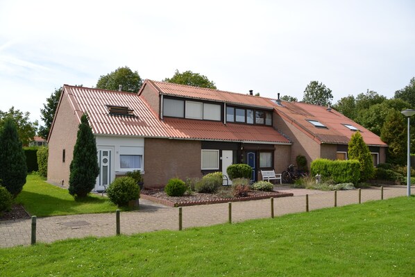 Une maison à deux étages avec un toit en pente, une porte d’entrée et un petit jardin agrémenté d’un banc et d’un vélo.