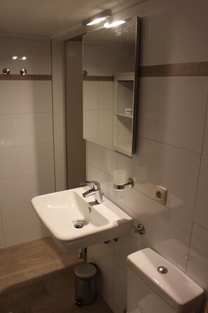 Une salle de bain avec un lavabo blanc, un miroir et des toilettes.