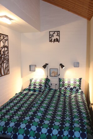 Une chambre à coucher avec un lit recouvert d’une couvre-lit à motifs, deux lampes de chevet, une horloge murale et un tableau encadré au-dessus du lit.