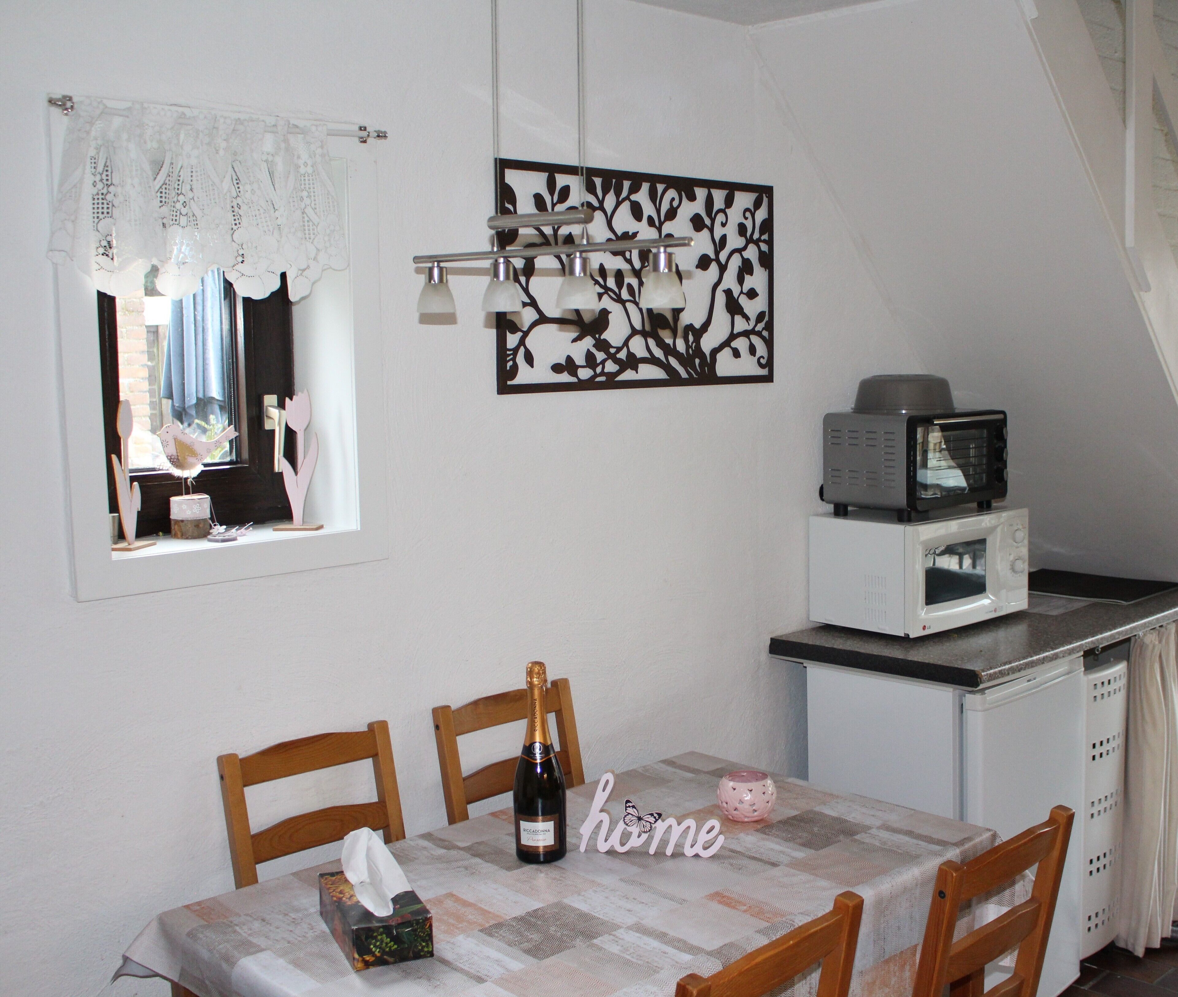 A dining area with a table set for two, a bottle of champagne, a tissue box, and a decorative sign.