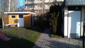 A small wooden structure with a door and window, a bench, and a red slide in a grassy area. - Bungalow 58 sqm, 300 m from the beach and subtropical bathing paradise, WLAN (Niedersachsen)