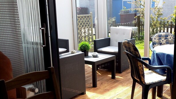 An open patio with wicker furniture, a small table with a plant, and a view of the backyard. - Bungalow 58 sqm, 300 m from the beach and subtropical bathing paradise, WLAN (Niedersachsen)