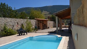 A swimming pool with a stone wall and a covered patio area. - Charming house with swimming pool (Montauban sur l'Ouveze)
