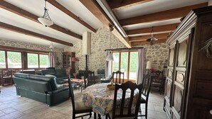 A spacious living area with a stone wall, wooden beams, a dining table with chairs, a sofa, and a television. - Charming house with swimming pool (Montauban sur l'Ouveze)