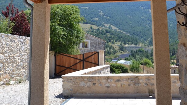 A covered outdoor area with a stone wall, wooden beams, and a view of a valley. - Charming house with swimming pool (Montauban sur l'Ouveze)