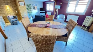 Un coin repas avec des chaises en osier, une table ronde en bois et une plante en pot aux fleurs roses.