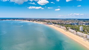 Paisagem costeira com uma praia arenosa, edifícios ao longo da costa e um céu azul e límpido.