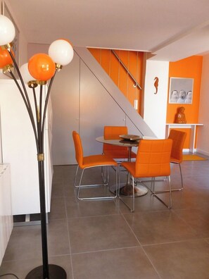 A modern dining area with orange chairs and a round table, a staircase with orange accents, and a decorative floor lamp.