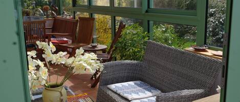 A cozy room with wicker furniture, a cushioned bench, and a vase of white orchids.