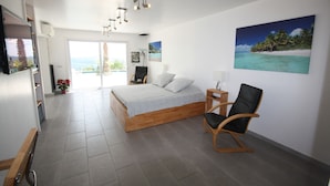 Un dormitorio con una cama de madera, una silla negra, un televisor y un cuadro de una playa.