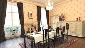 A dining room with a table set for four, a chandelier, and a view through a window with curtains.