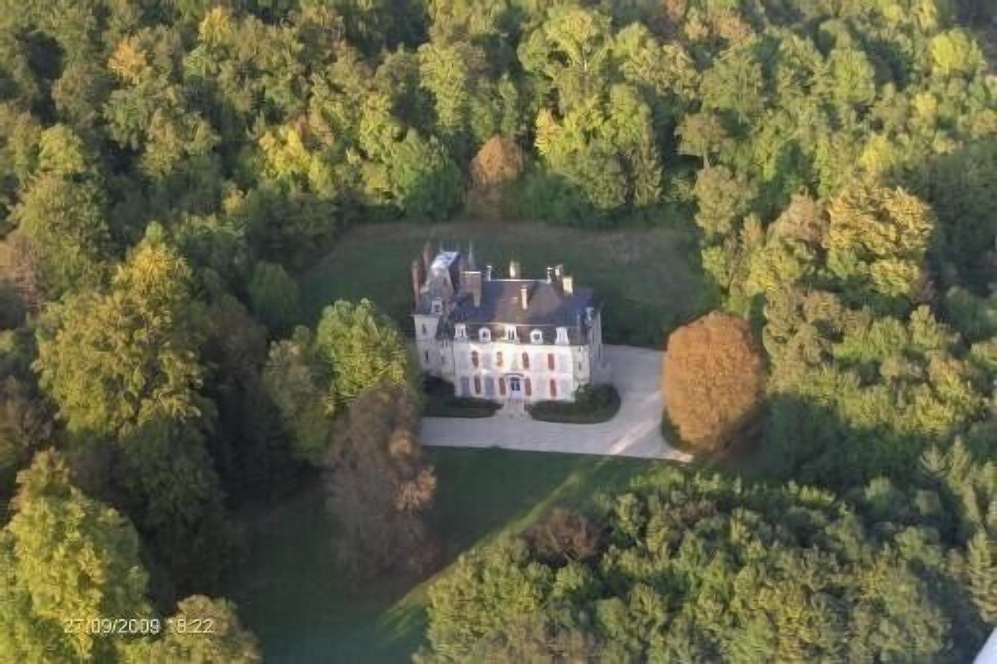 An aerial view of a large, historic mansion surrounded by dense forest.