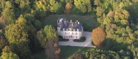 An aerial view of a large, historic mansion surrounded by dense forest.