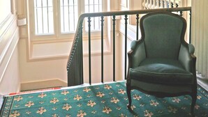 A staircase with a green chair, a white-framed window, and a mirror.