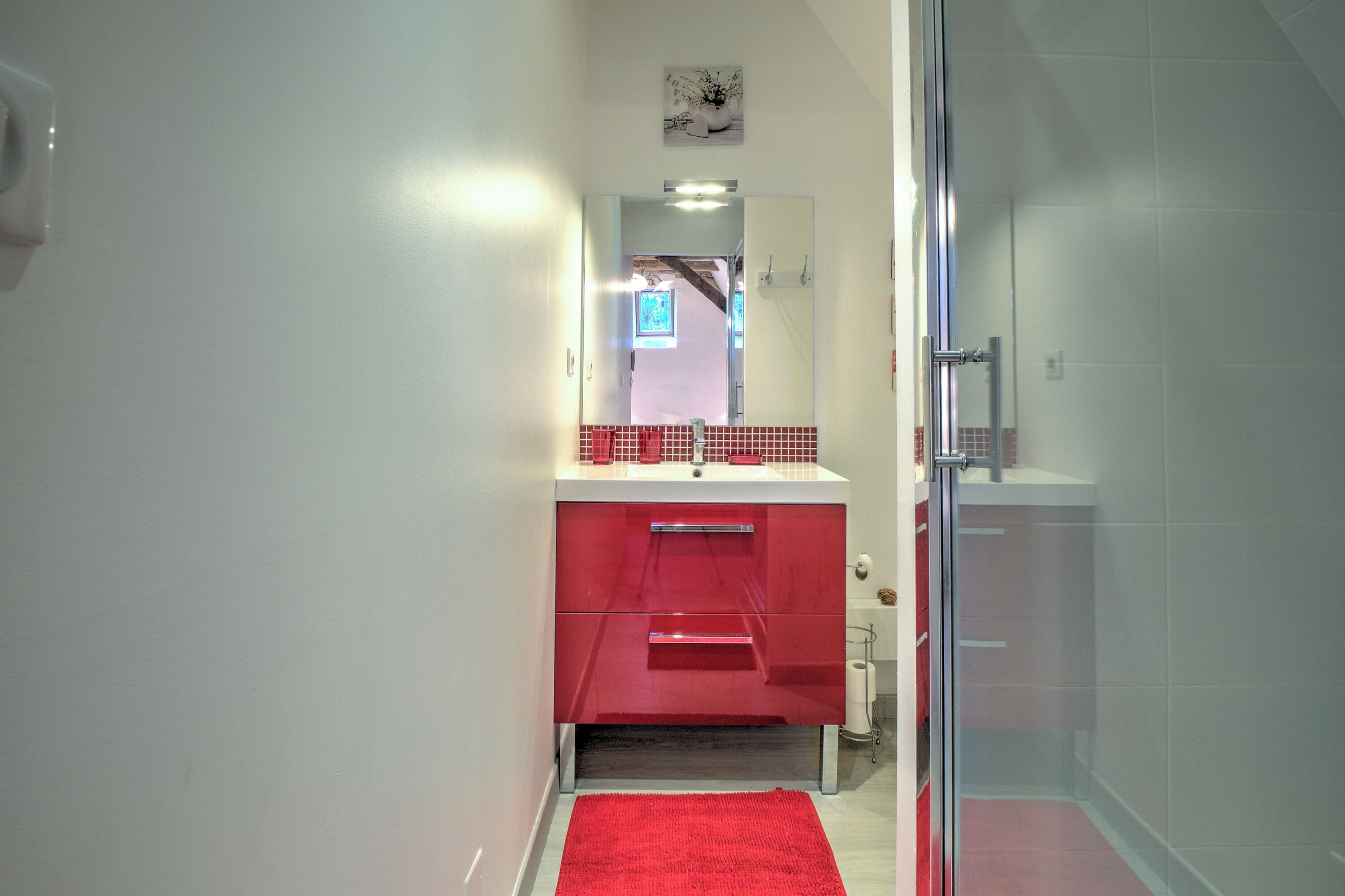 Ein Badezimmer mit einem roten Waschbecken, weißen Wänden und einer Duschkabine aus Glas.