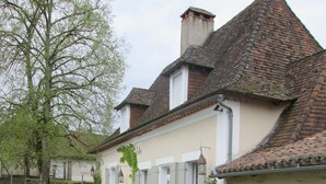 A traditional European-style house with a garden in front, featuring a stone wall, flowering plants, and a metal gate. - Moulin de Villeverneix and its tower, Neuvic on the banks of the Vern for 6, 8 people (Neuvic)