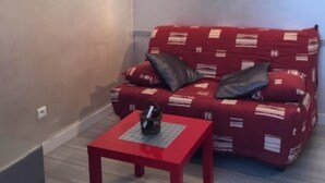 Un espacio de sala pequeño y acogedor con un sofá rojo, dos almohadas, una mesita roja y un cuadro en la pared.