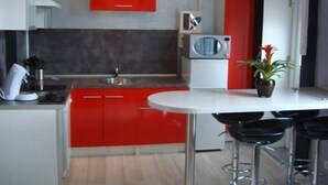 Una cocina moderna con armarios rojos, una encimera blanca, microondas y fregadero. Hay tres taburetes negros y una planta en maceta.
