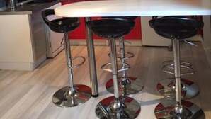 Una cocina moderna con encimera blanca, detalles en rojo y taburetes de barra de acero inoxidable.