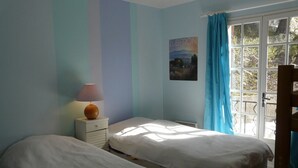A bedroom with two beds, a nightstand with a lamp, a window with curtains, and a poster on the wall. - Quiet holiday villa with swimming pool and superb view in the Luberon (Vitrolles-En-Lubéron)