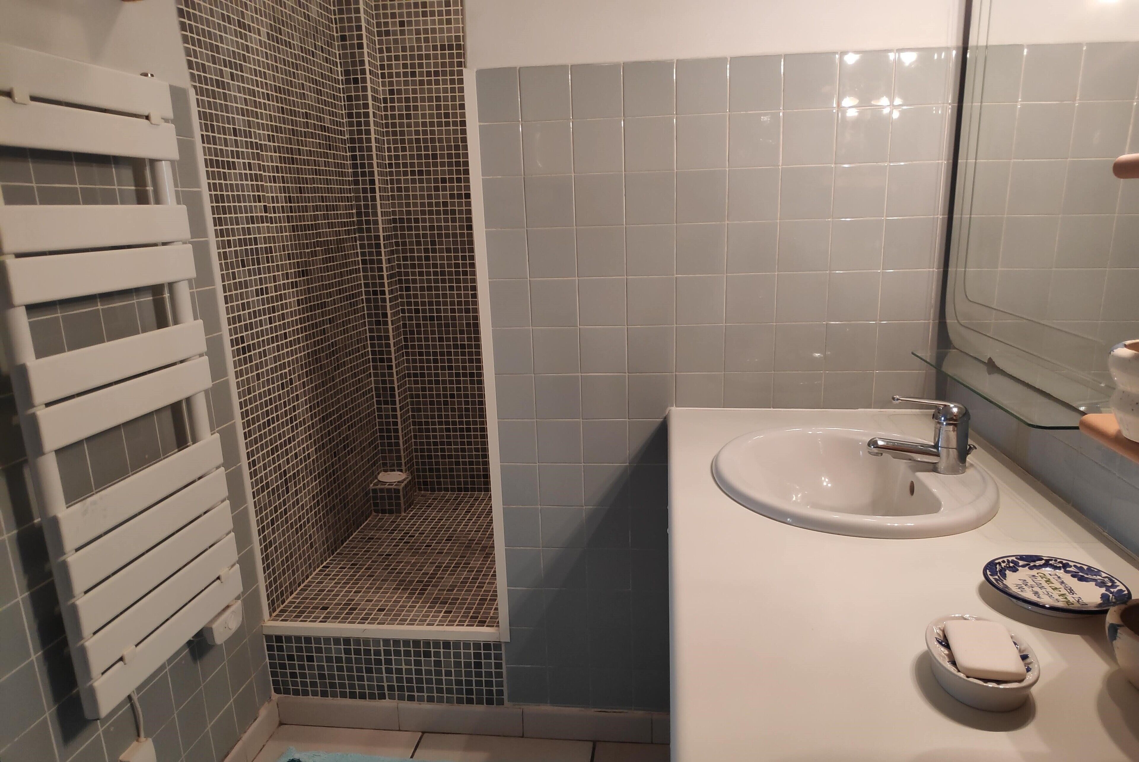 Un baño con lavamanos blanco, un espejo y una zona de ducha con paredes de azulejos.