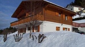 Una cabaña de madera con balcón, rodeada de nieve y árboles.